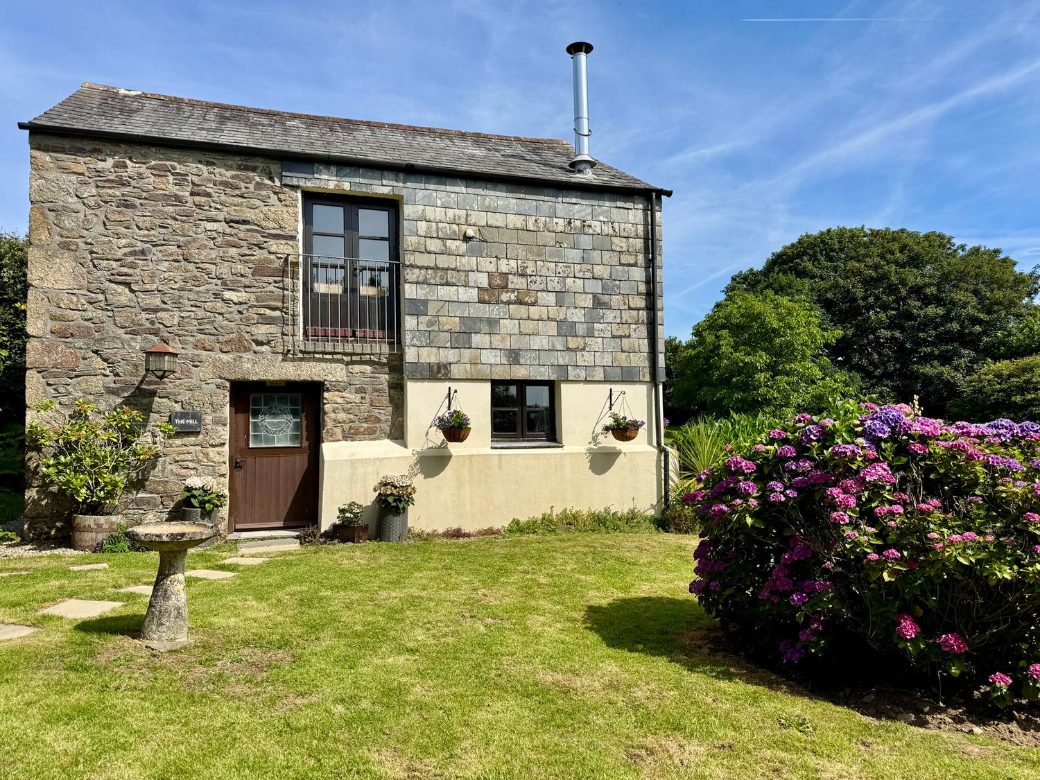 An outdoor view of a stone building with a slate roof and garden at The Mill in Lostwithiel