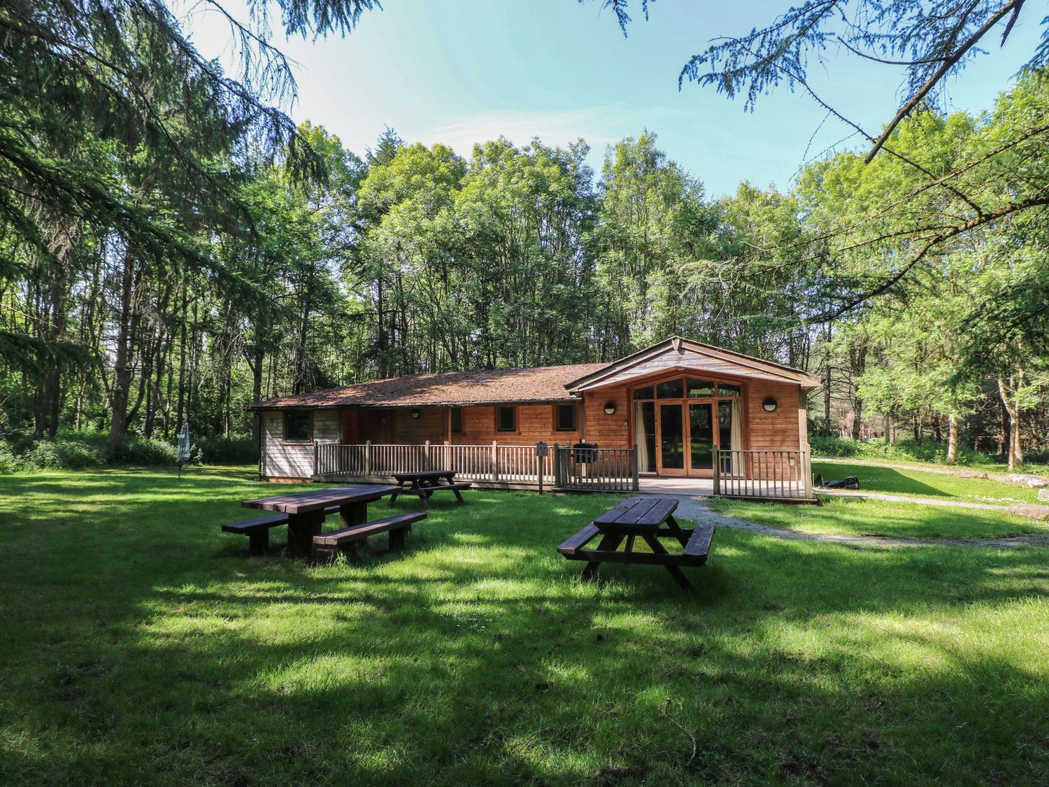 A wooden lodge surrounded by trees with picnic tables on grass at Chestnut Lodge in Rosliston