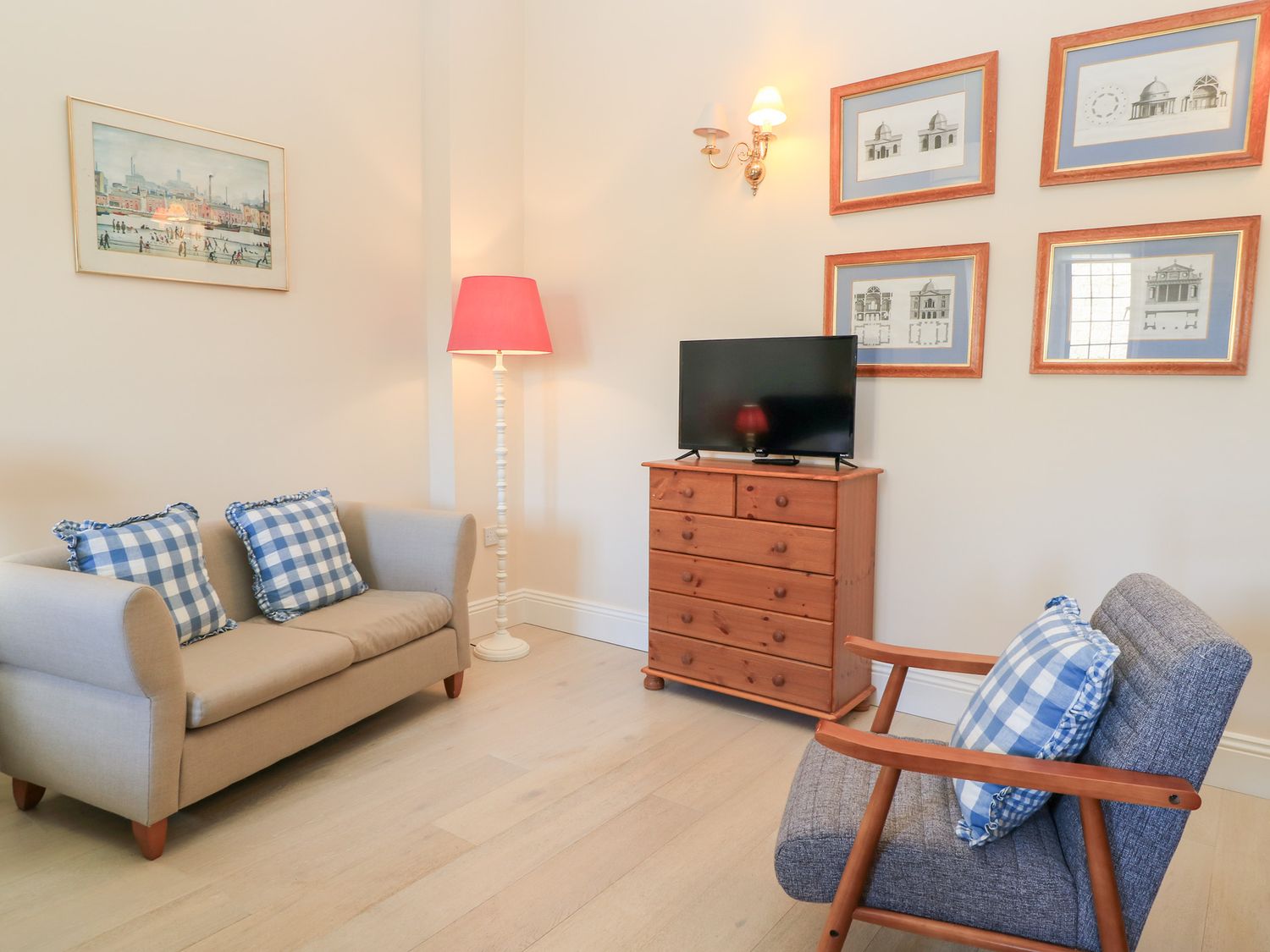 A sitting room with a beige sofa and blue checkered cushions a wooden chest of drawers with a TV on top and a grey armchair with a blue checkered cushion at Swallow Studio in Andoversford near Cheltenham