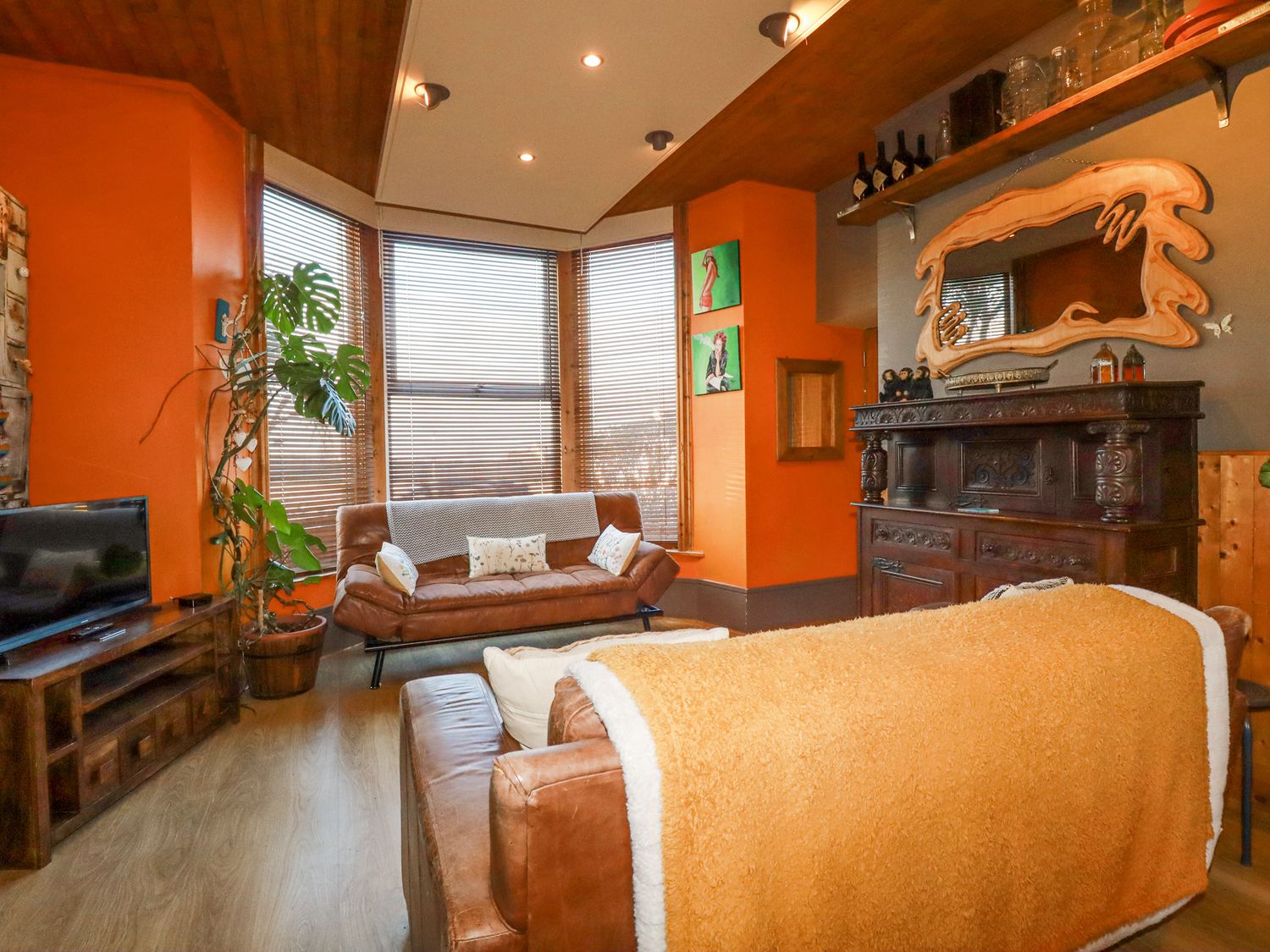 A living room with leather sofas a wooden cabinet a large plant a TV and windows with blinds at Mermaid's Rest in Newquay