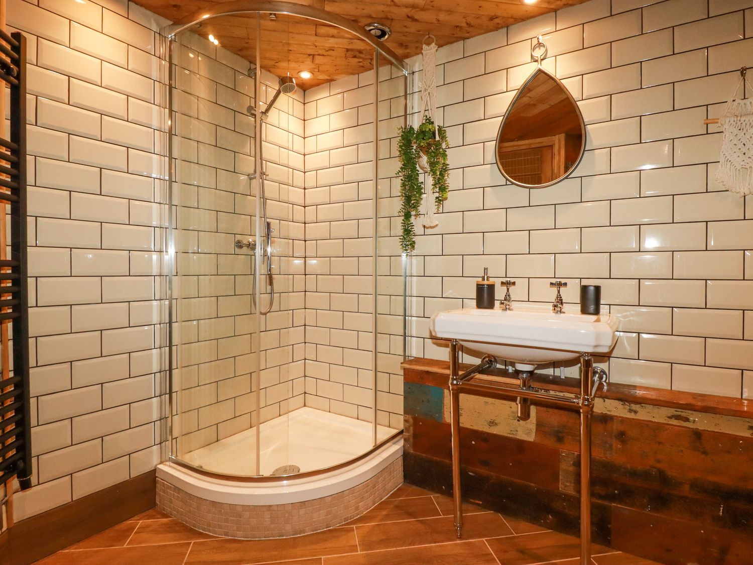 A bathroom with a corner shower enclosure a white sink a round mirror and hanging plants at Mermaid's Rest in Newquay