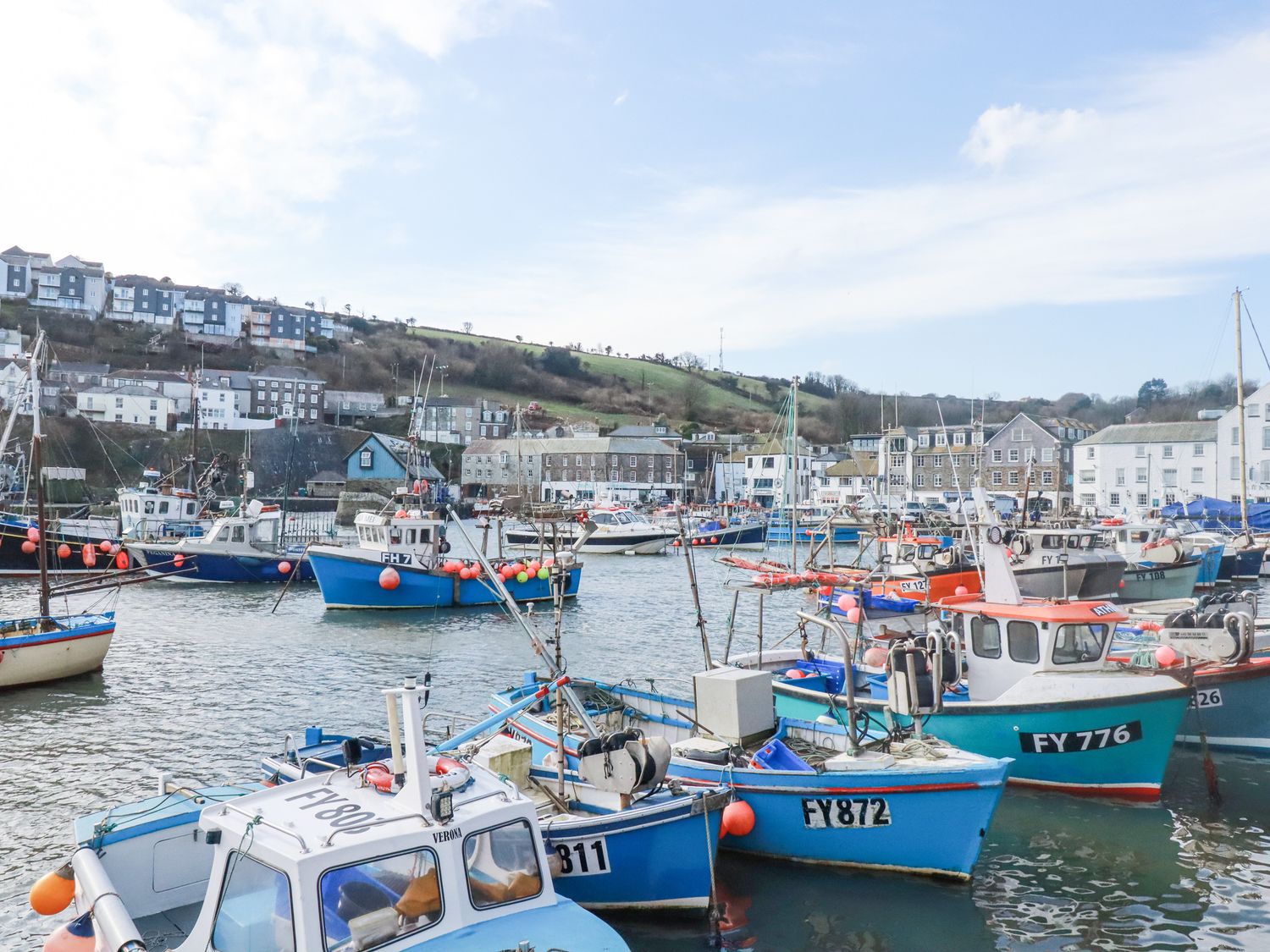 Fishing boats docked in a harbor with buildings and hills in the background at Oystercatcher Mevagissey