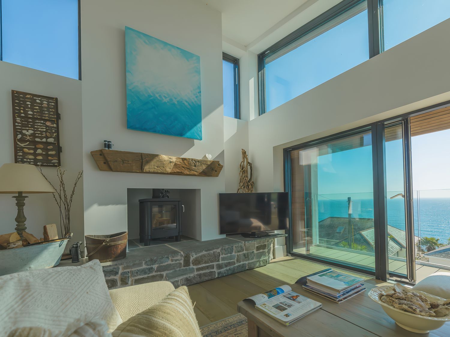 A living room with a wood stove TV and large windows overlooking the sea at Oystercatcher in Mevagissey
