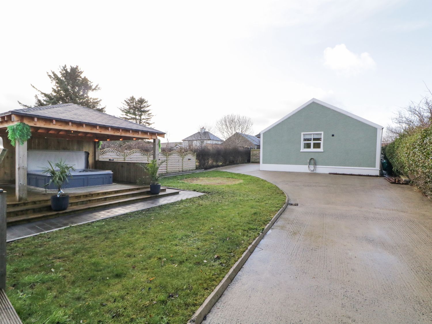 A backyard with a covered wooden hot tub area and a driveway leading to a single-story house at Woodside Guest House in Castlerock