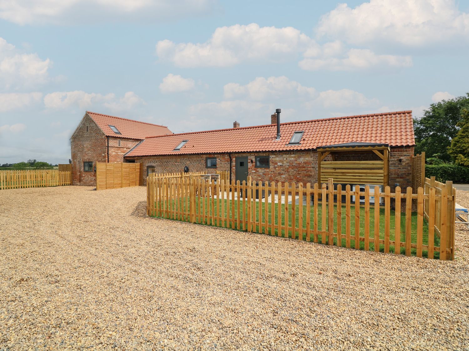 An outdoor view of a house with a fence and gravel at Buzzard Barn in Woodhall Spa