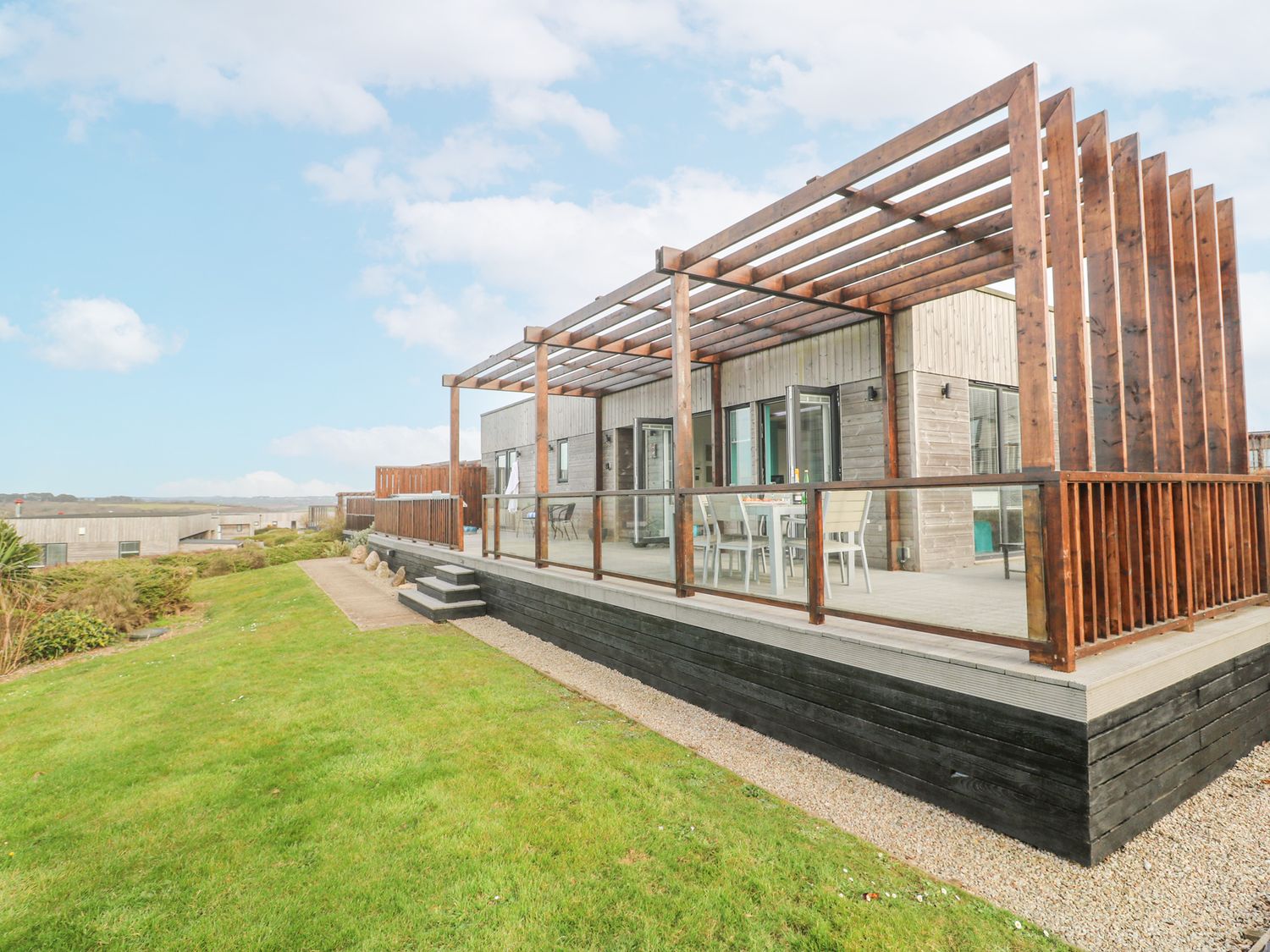 A wooden deck with a pergola and outdoor dining furniture next to a grassy area at Hepworth in Portreath
