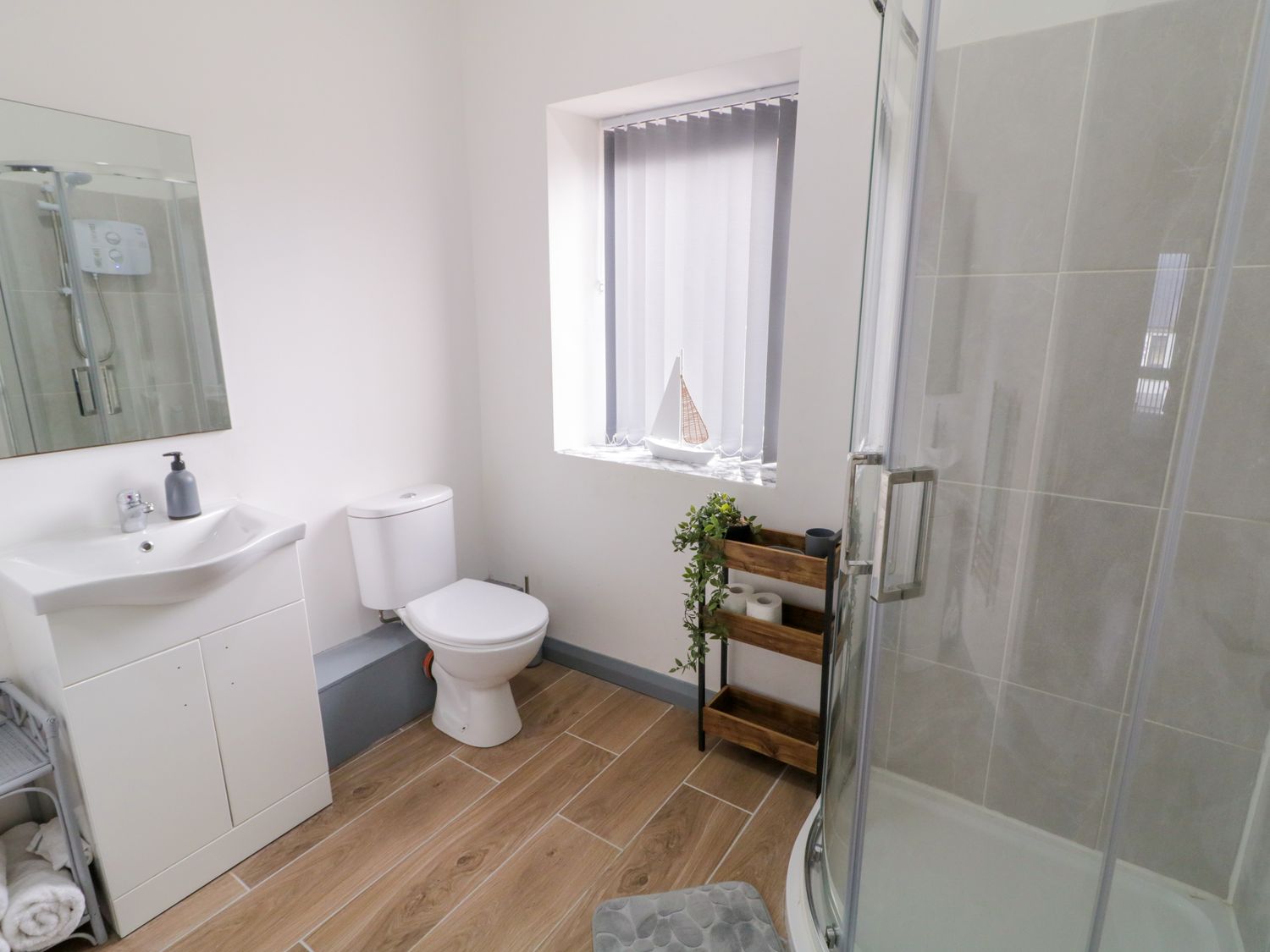 A bathroom with a sink and mirror toilet a window with blinds a wooden shelf and a glass shower at Town House No 1 in Falcarragh County Donegal