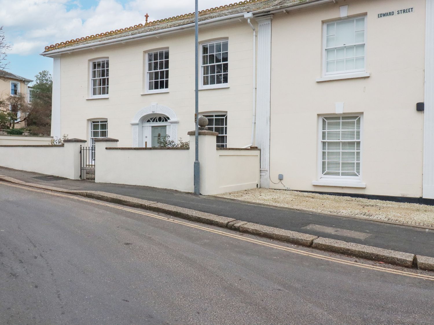 A street view of a beige two story house with white framed windows and a small front yard on Edward Street at Rhondda House in Truro