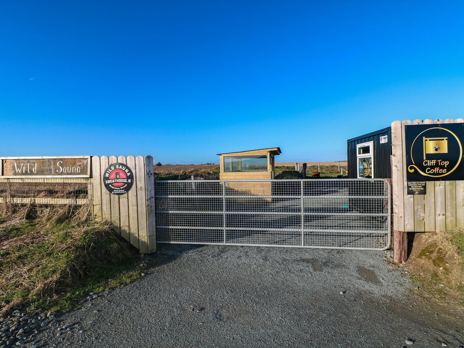 An entrance gate with signs for wild sauna and cliff top coffee in an outdoor setting at Beach Row in Fethard-On-Sea
