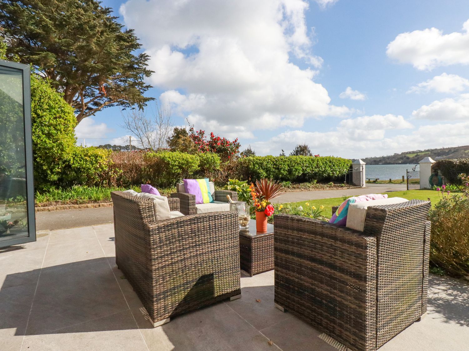An outdoor patio with wicker chairs and a table near a garden and water at Turnstones Point near Carnon Downs