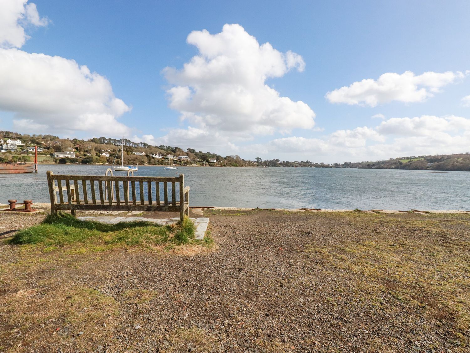 A wooden bench facing a body of water with houses and boats in the background at Turnstones Point near Carnon Downs