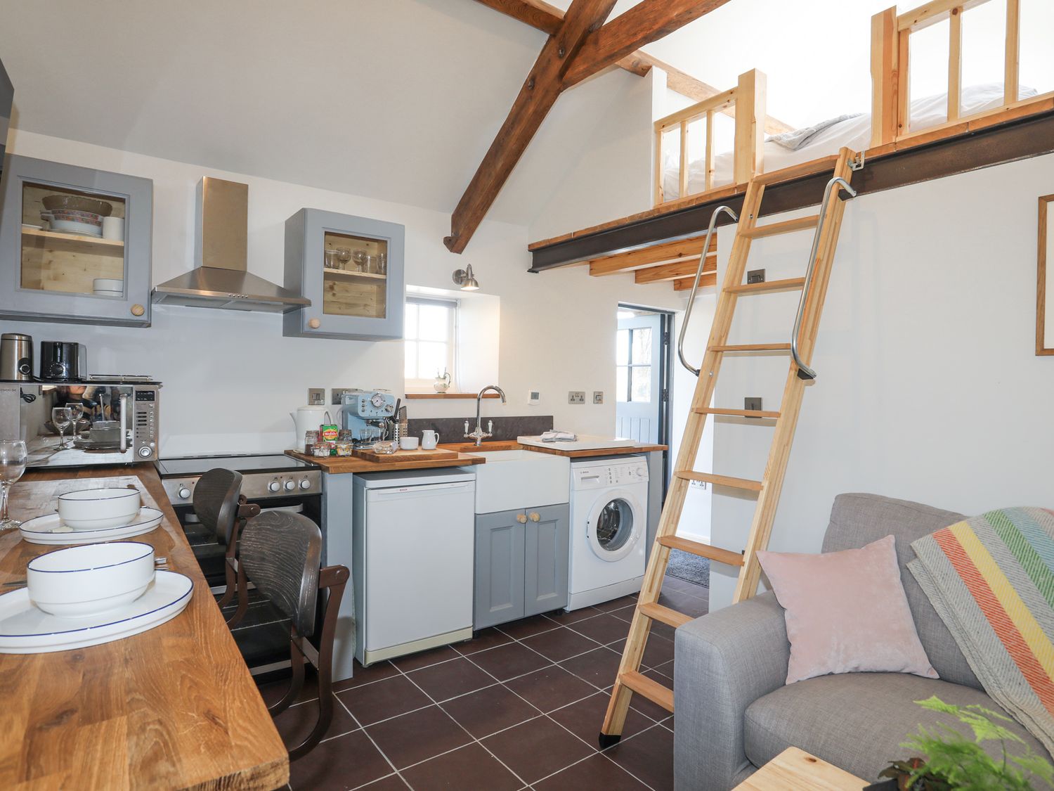 A kitchen with wood countertops a ladder leading to a loft and a gray sofa at Cwt Mochyn in Llanberis