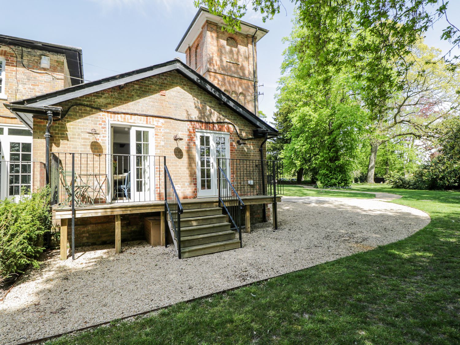A gravel path leading to a brick building with two white doors and a small porch surrounded by green trees at Cedar in Elcot near Newbury
