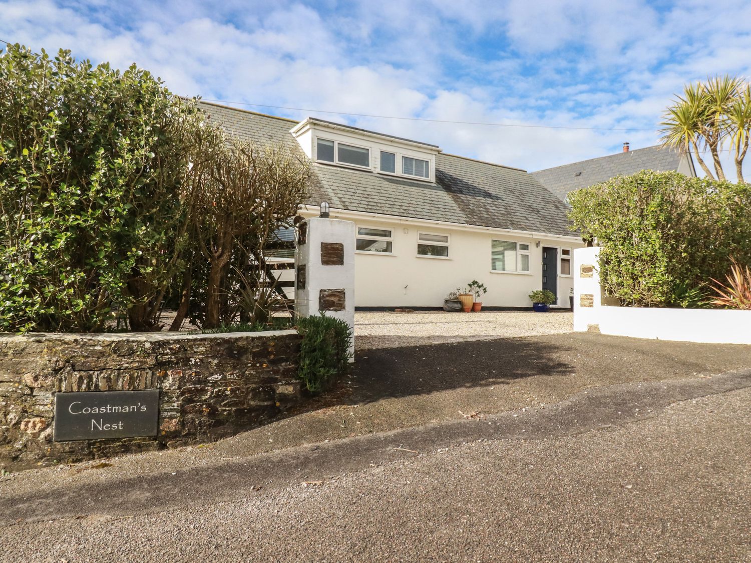 A white house with a grey roof and gravel driveway surrounded by bushes at Coastmans Nest in Mawgan Porth