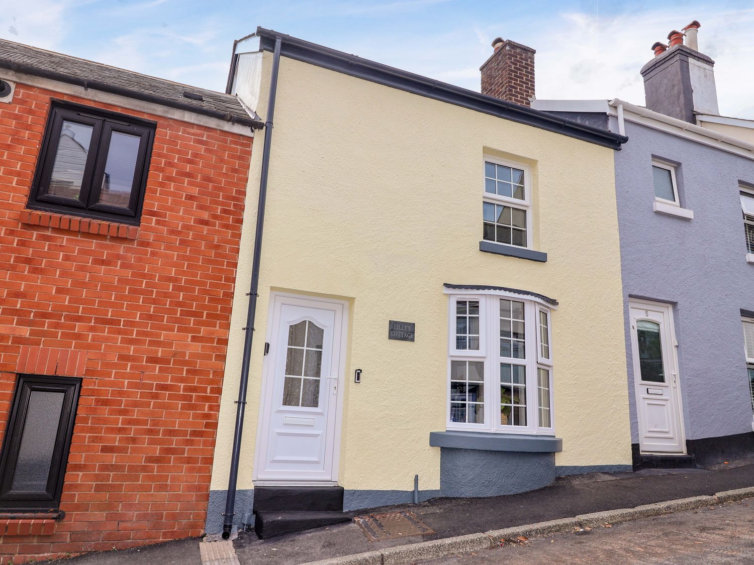 A yellow house with a white door and windows at Lilly's Cottage in Dawlish