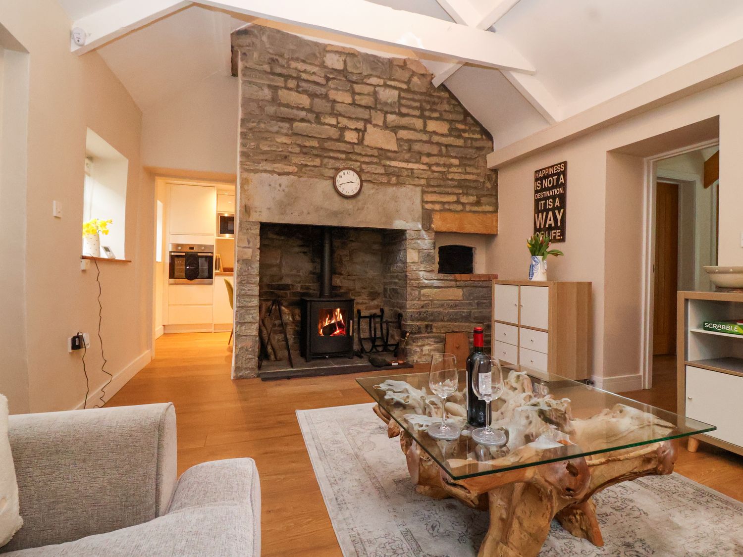 A living room with a stone fireplace and a wood burning stove a glass coffee table with a bottle of wine and glasses a sofa and a chest of drawers at Honeysuckle Cottage in Compton Dundon near Street