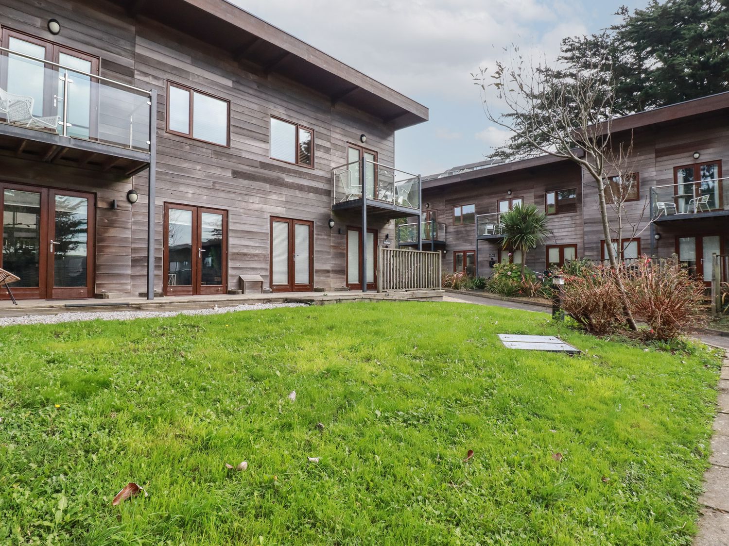 An outdoor area with green grass and wooden buildings with balconies at Treveglos in Porthtowan