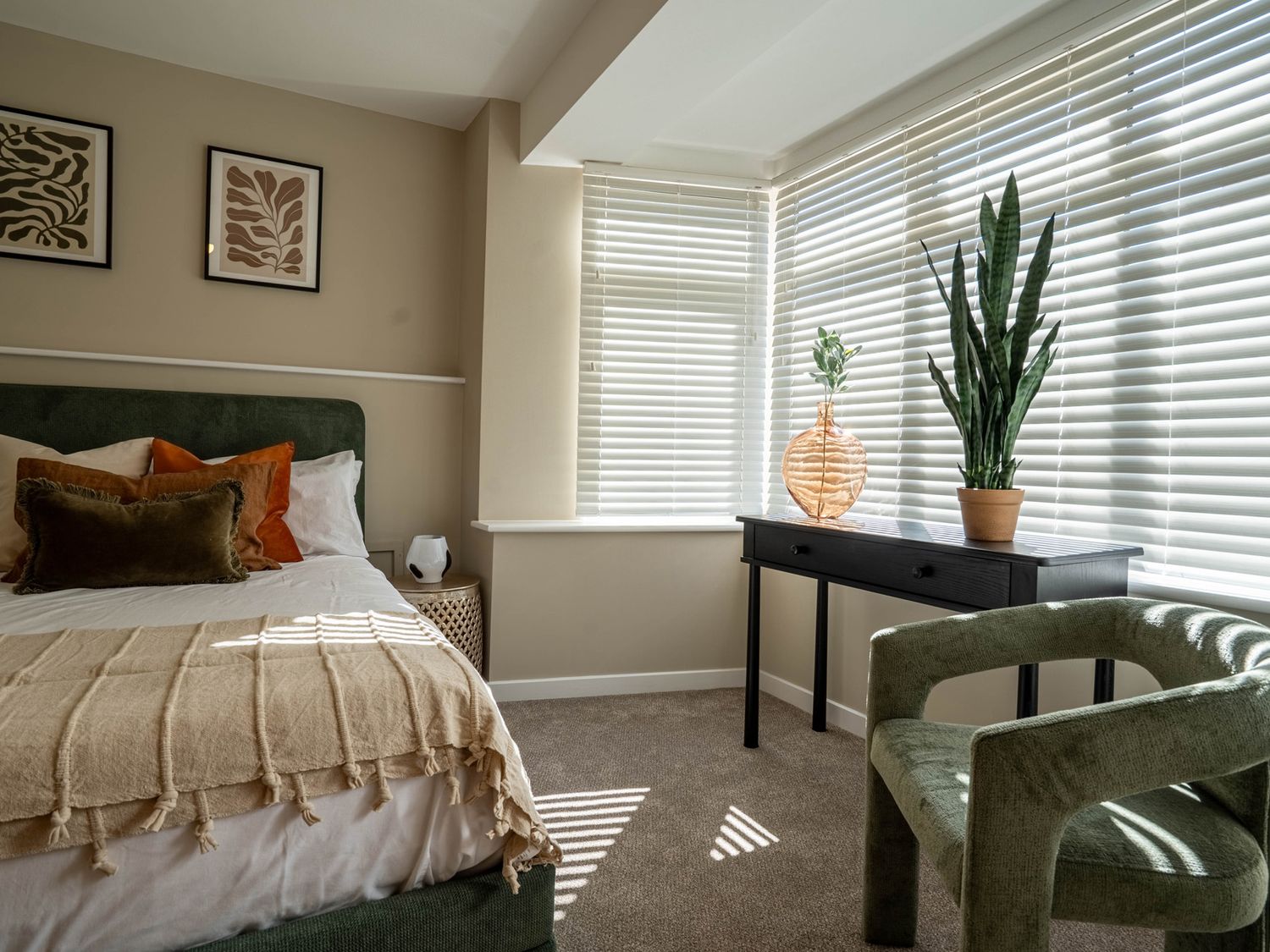 A bedroom with a bed pillows and blanket a black table with plants and a green chair by a window with blinds at The Reef in Kessingland
