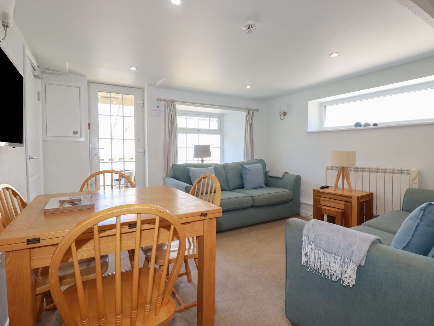 A room with two blue sofas a wooden dining table with four chairs a side table with lamp and windows at St Saviours in Padstow