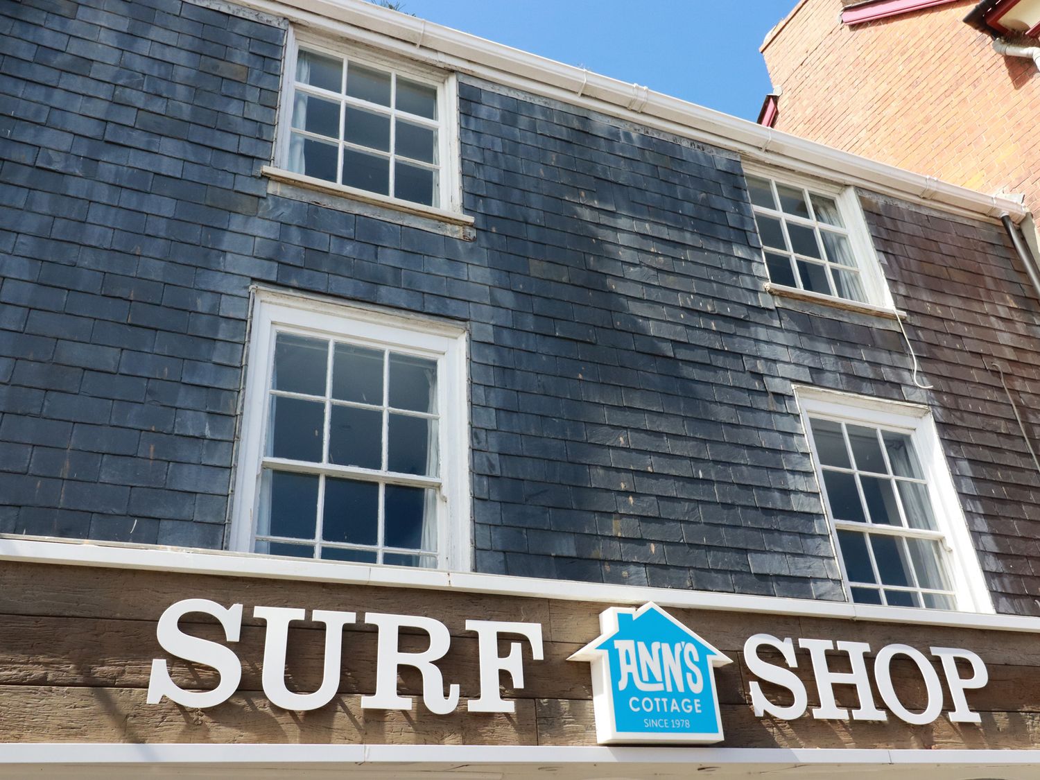 The front of a building with four windows and a surf shop sign with a blue house logo at St Saviours in Padstow