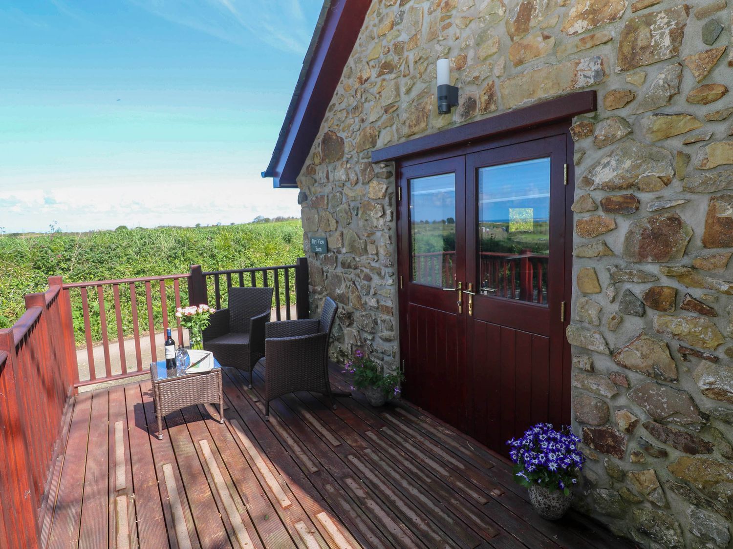 A wooden deck with rattan chairs and a table outside a stone building at Bay View Barn in Hayle