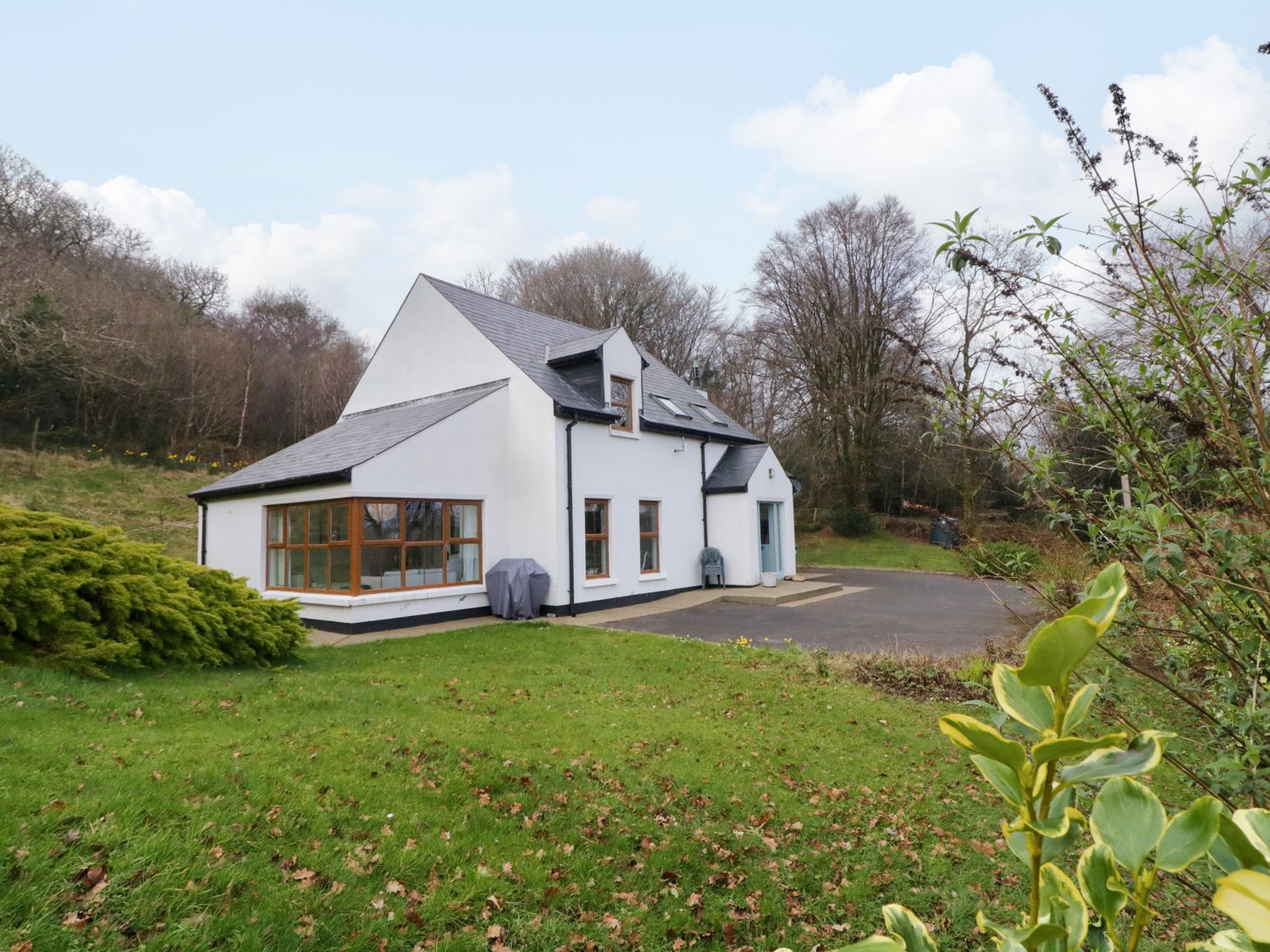 A white two-story house with a gray roof and large windows surrounded by grass and trees at Clondallon Cottage in Clondallon near Rathmullan County Donegal