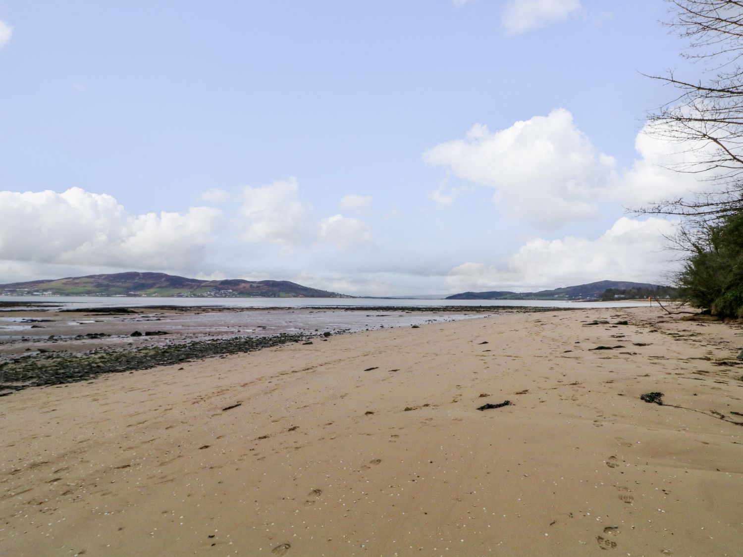 A sandy beach with footprints and seaweed with hills and water in the background at Clondallon Cottage in Clondallon near Rathmullan County Donegal
