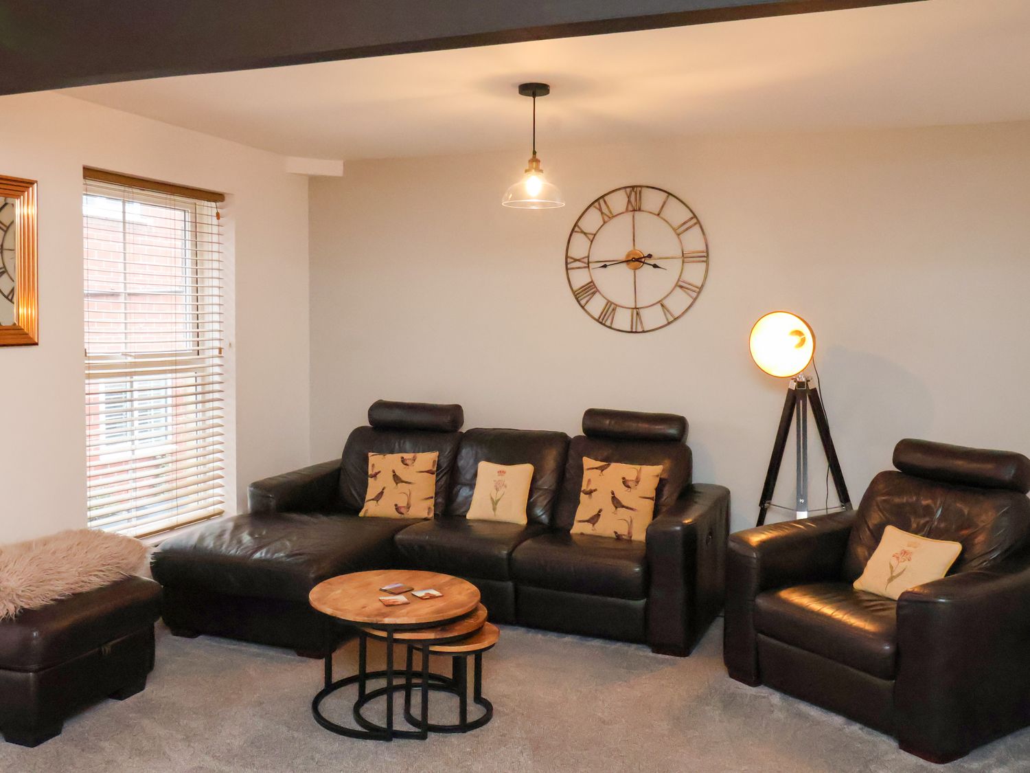 A living room with leather sofas a round wooden coffee table a floor lamp and a wall clock at The Arches in Whitby