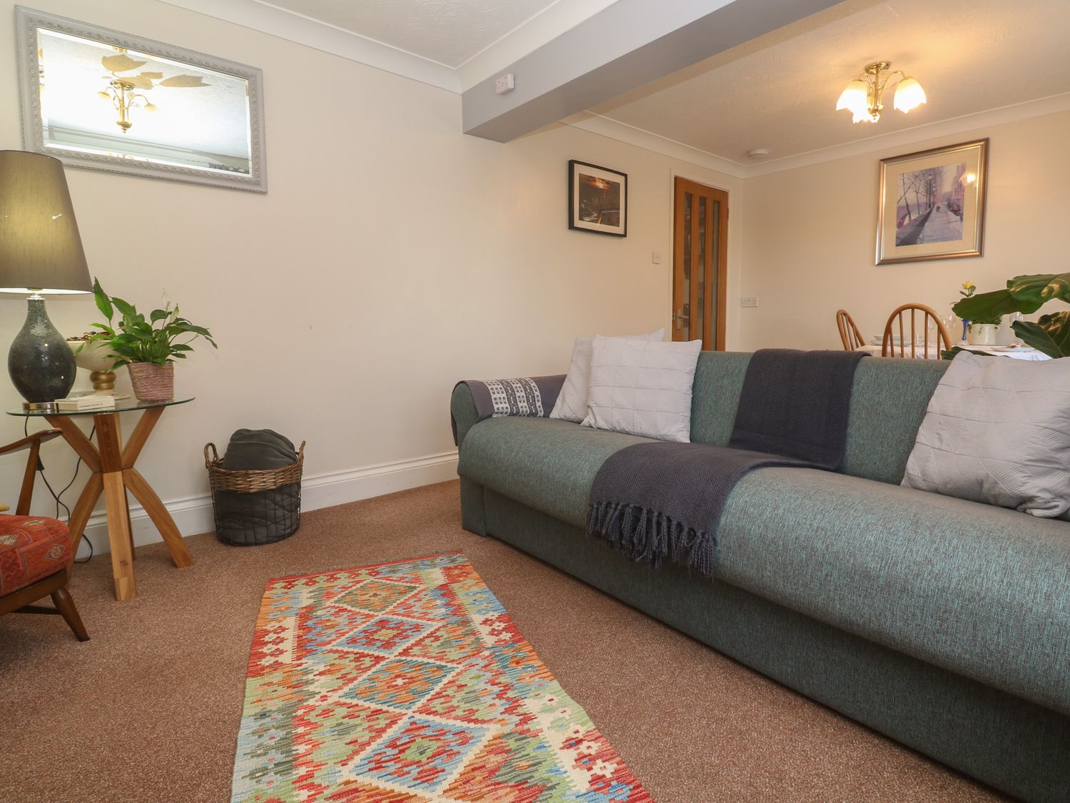 A living room with a green sofa pillows a colorful rug and a side table with a lamp and plants at Ty Metheven in Camborne
