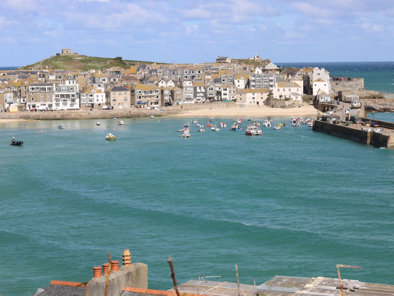 A coastal town with houses along the shoreline a sandy beach boats in the water and a pier extending into the sea at Ty Metheven in Camborne