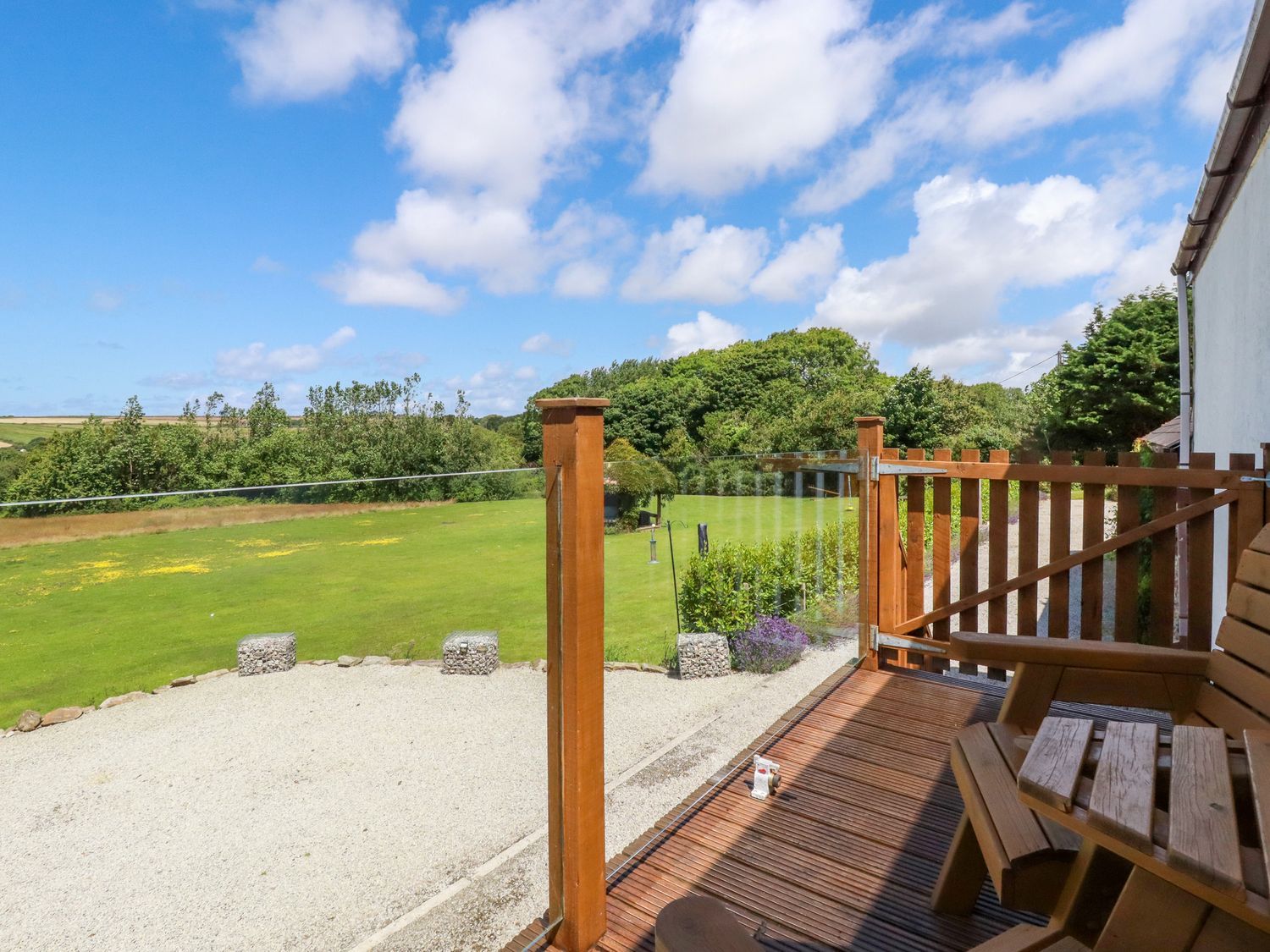 A wooden balcony with chairs overlooking a green lawn and trees at Meadows Edge in Perranwell near Goonhavern