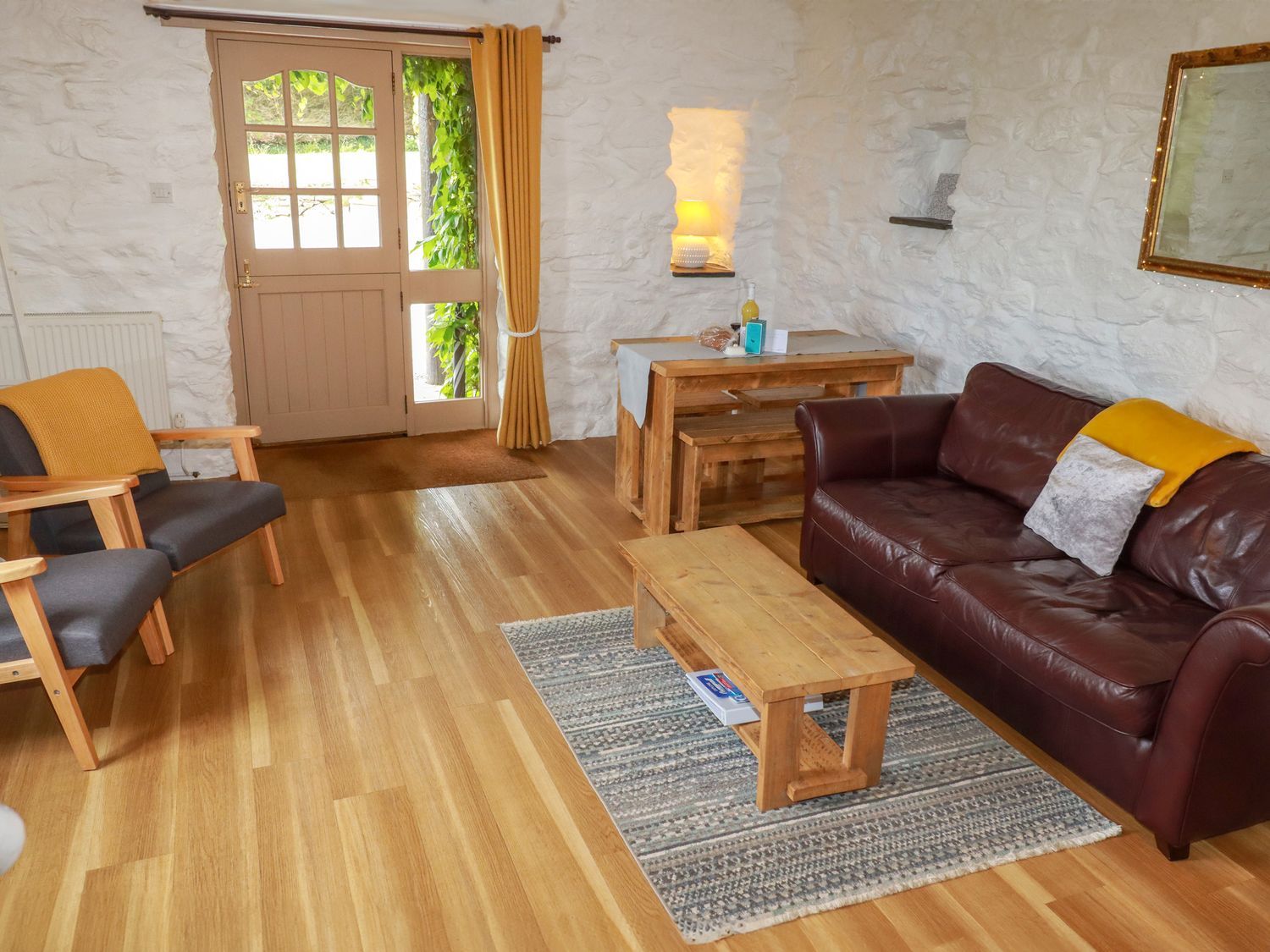 A sitting room with wooden table and chairs a brown leather sofa and a door with windows at Babes Cottage in Perranwell near Goonhavern