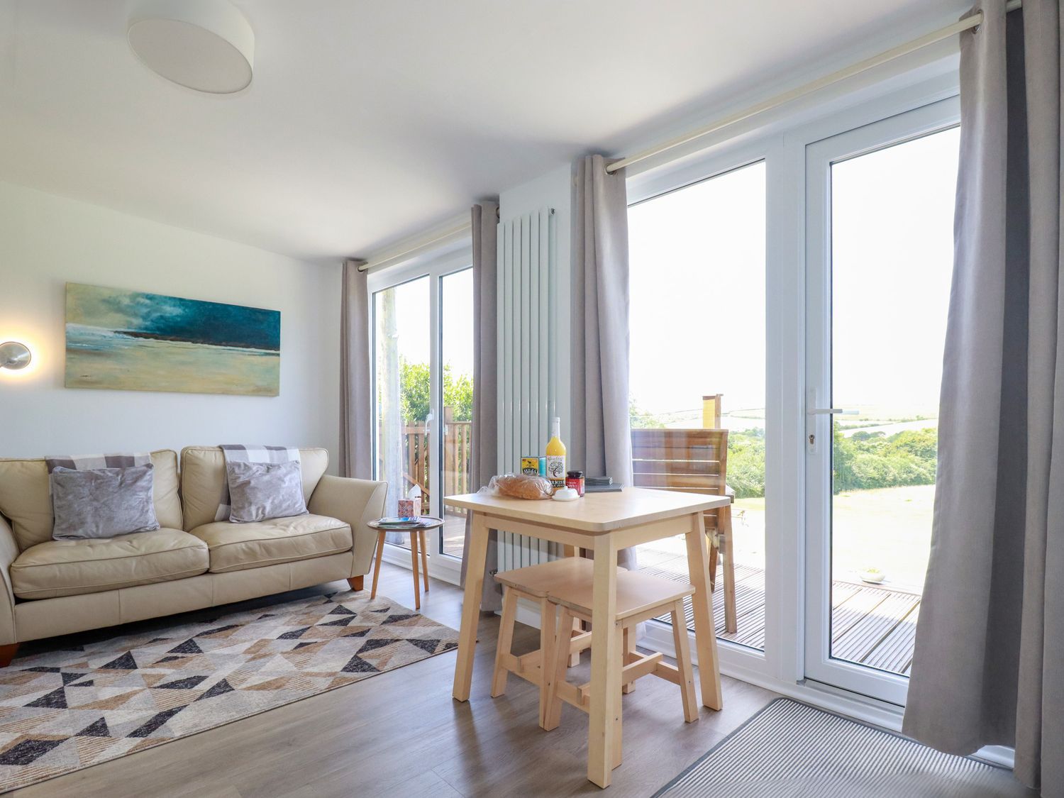 A living room with a beige sofa a wooden dining table and large glass doors at The Lookout in Perranwell near Goonhavern