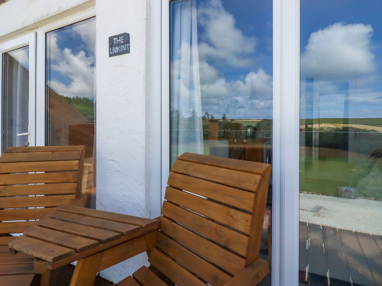 Wooden chairs and table outside glass doors with a sign reading The Lookout at The Lookout in Perranwell near Goonhavern