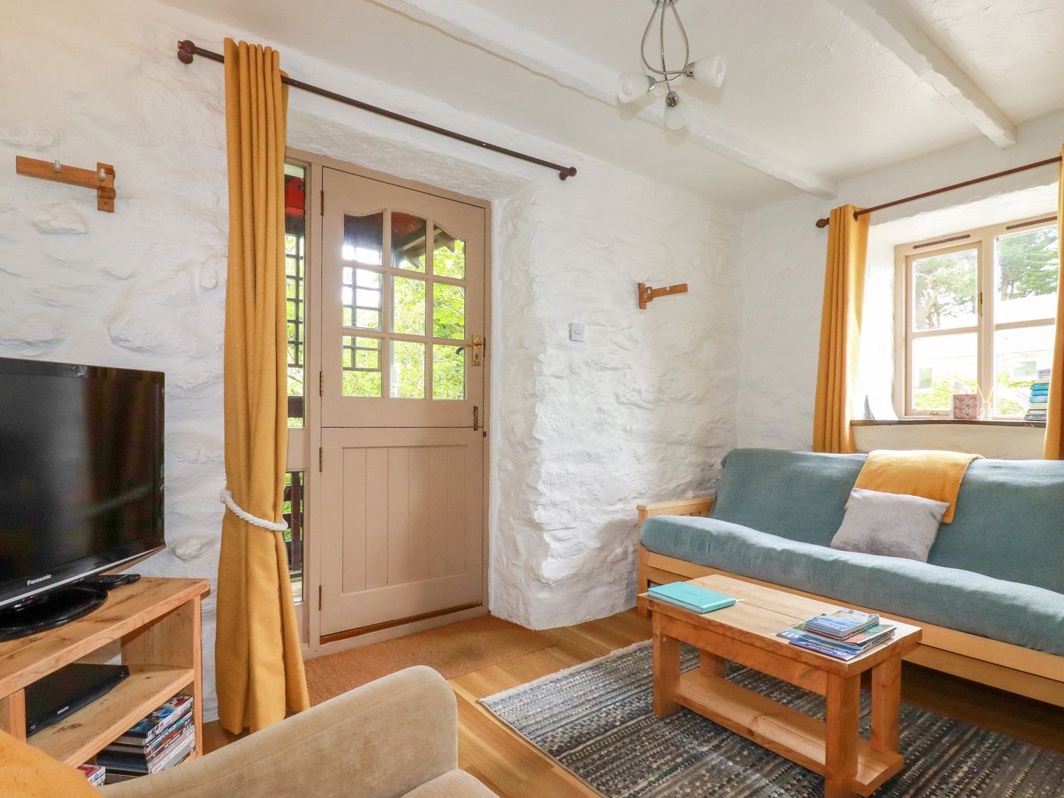 A sitting room with a blue sofa wooden coffee table and television at Hollies Cottage Perranwell near Goonhavern