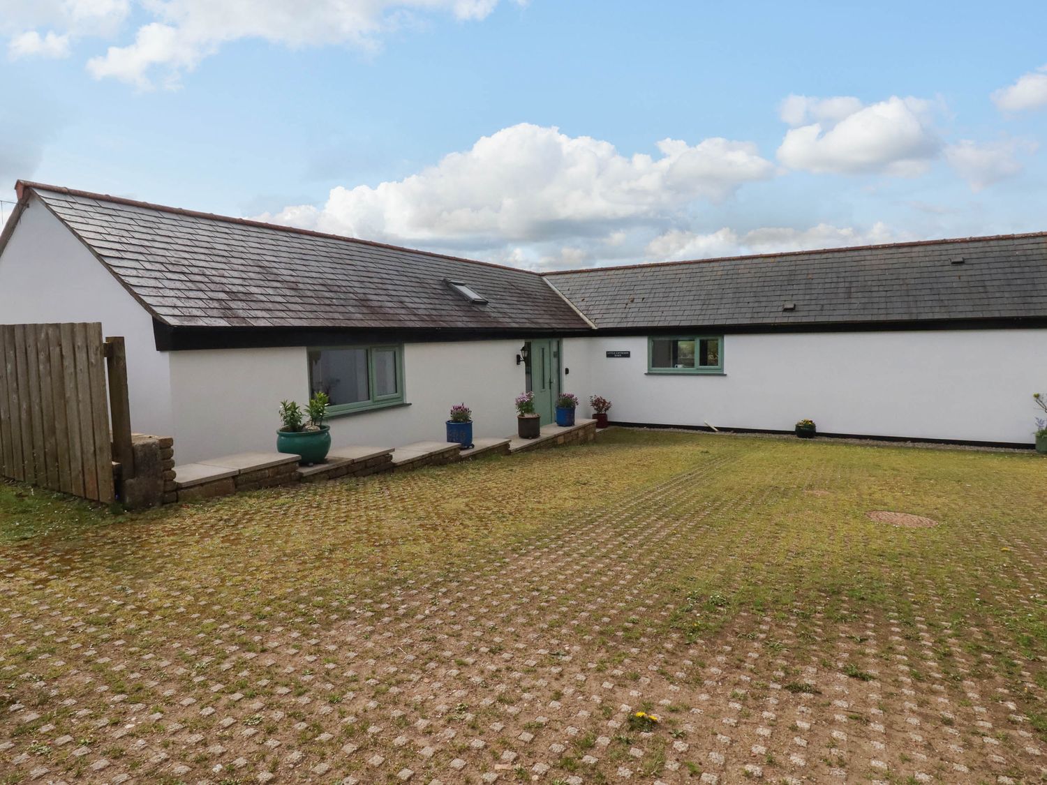 A white single-story house with green window frames and potted plants in front at Little Chywoon Barn in Truro