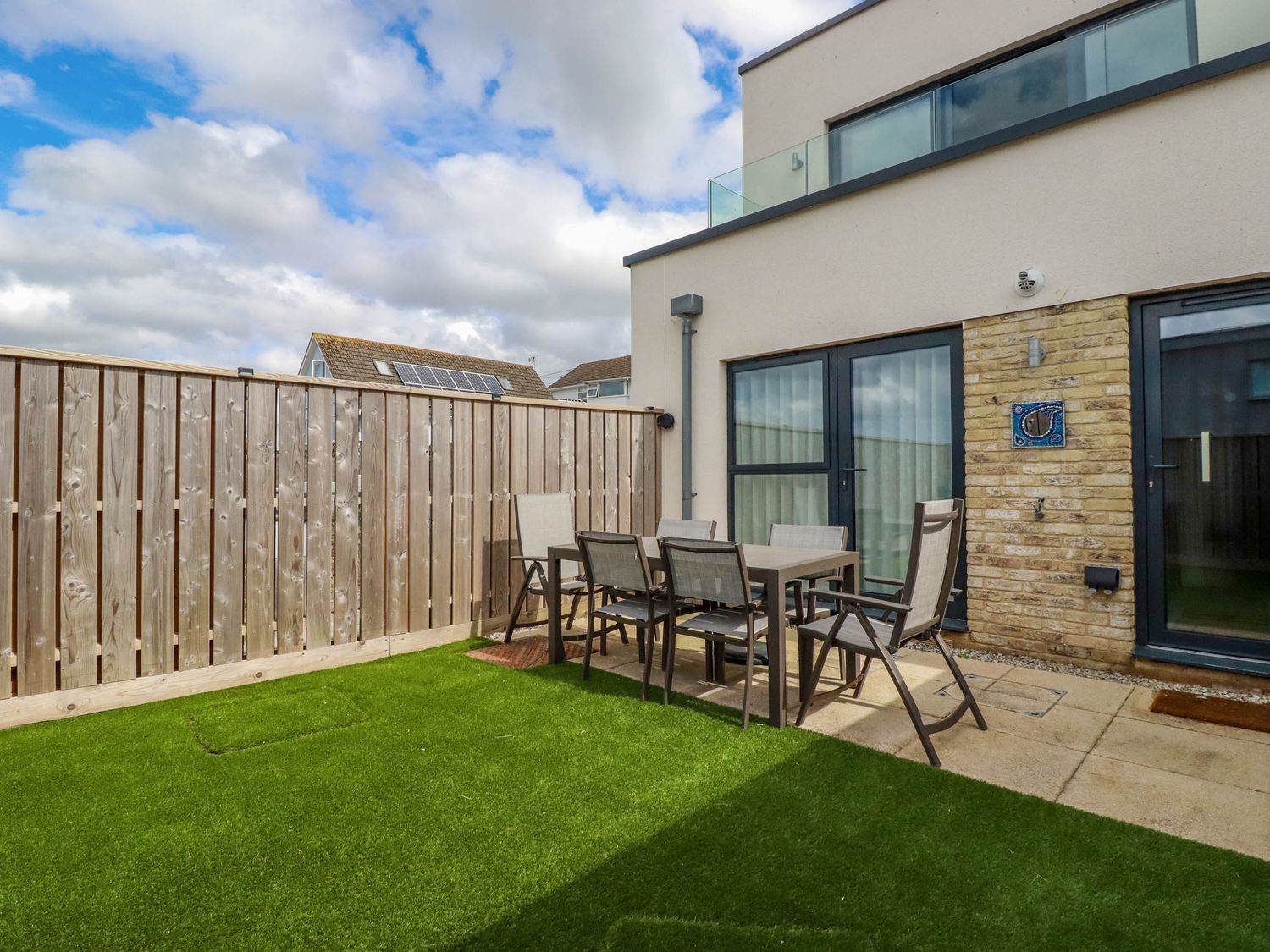 An outdoor patio area with a dining table and six chairs on artificial grass at Ebbtide in Newquay