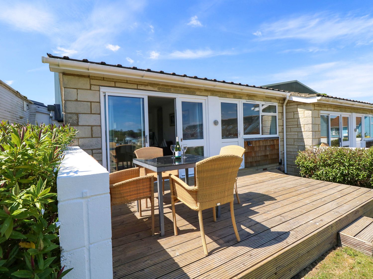 An outdoor wooden deck with a table and four wicker chairs outside a stone house at Cape 14 in Yarmouth