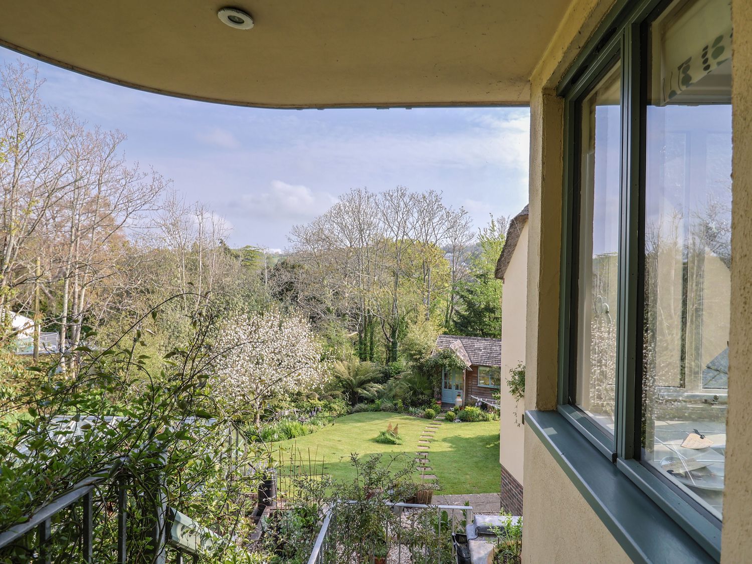 A balcony view overlooking a garden with a lawn path leading to a small wooden shed surrounded by trees at Bentley Rise Lyme Regis