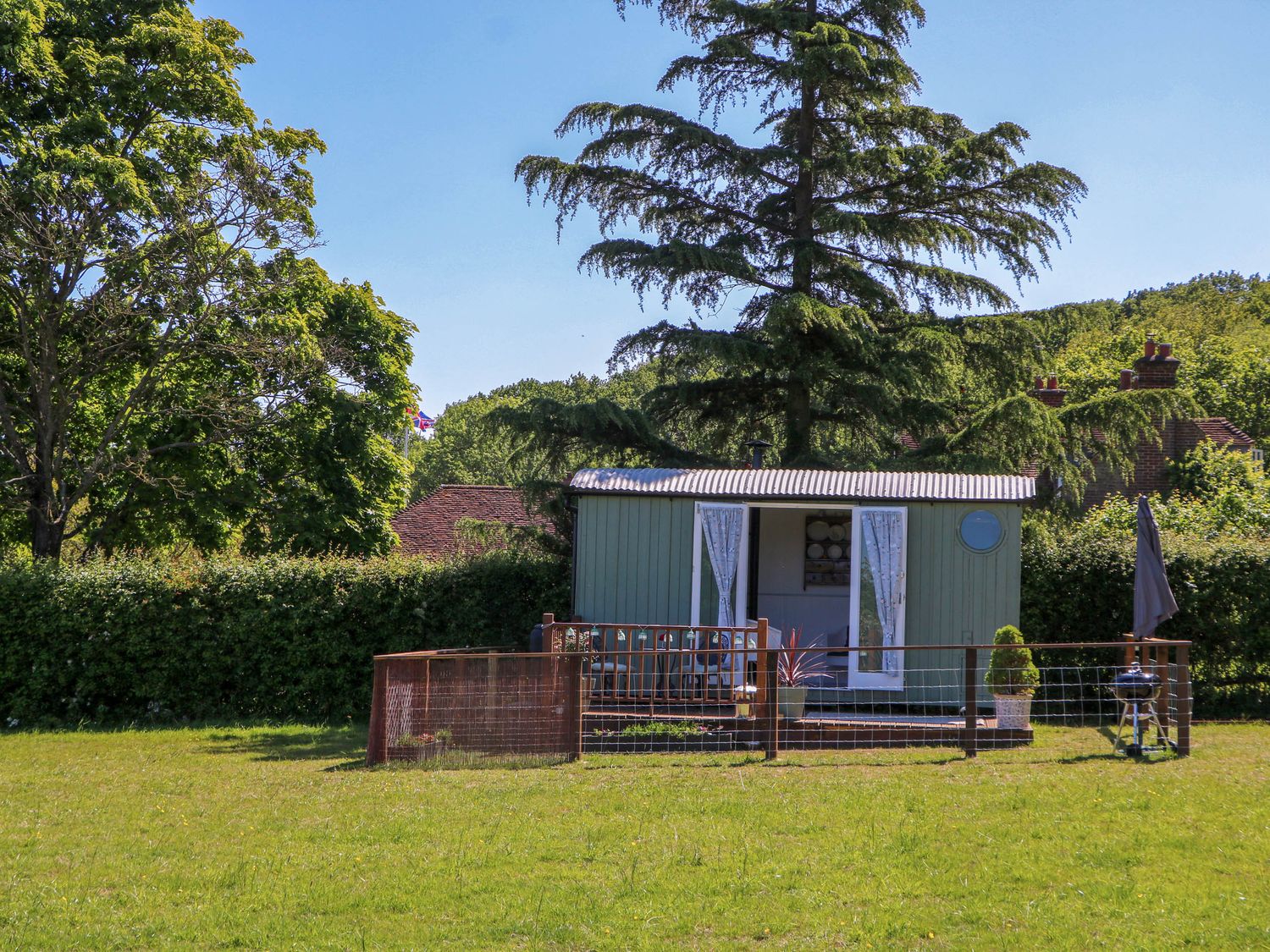 A small garden shed with open doors and a fenced grassy yard surrounded by trees at Songbirds in St Michaels Kent