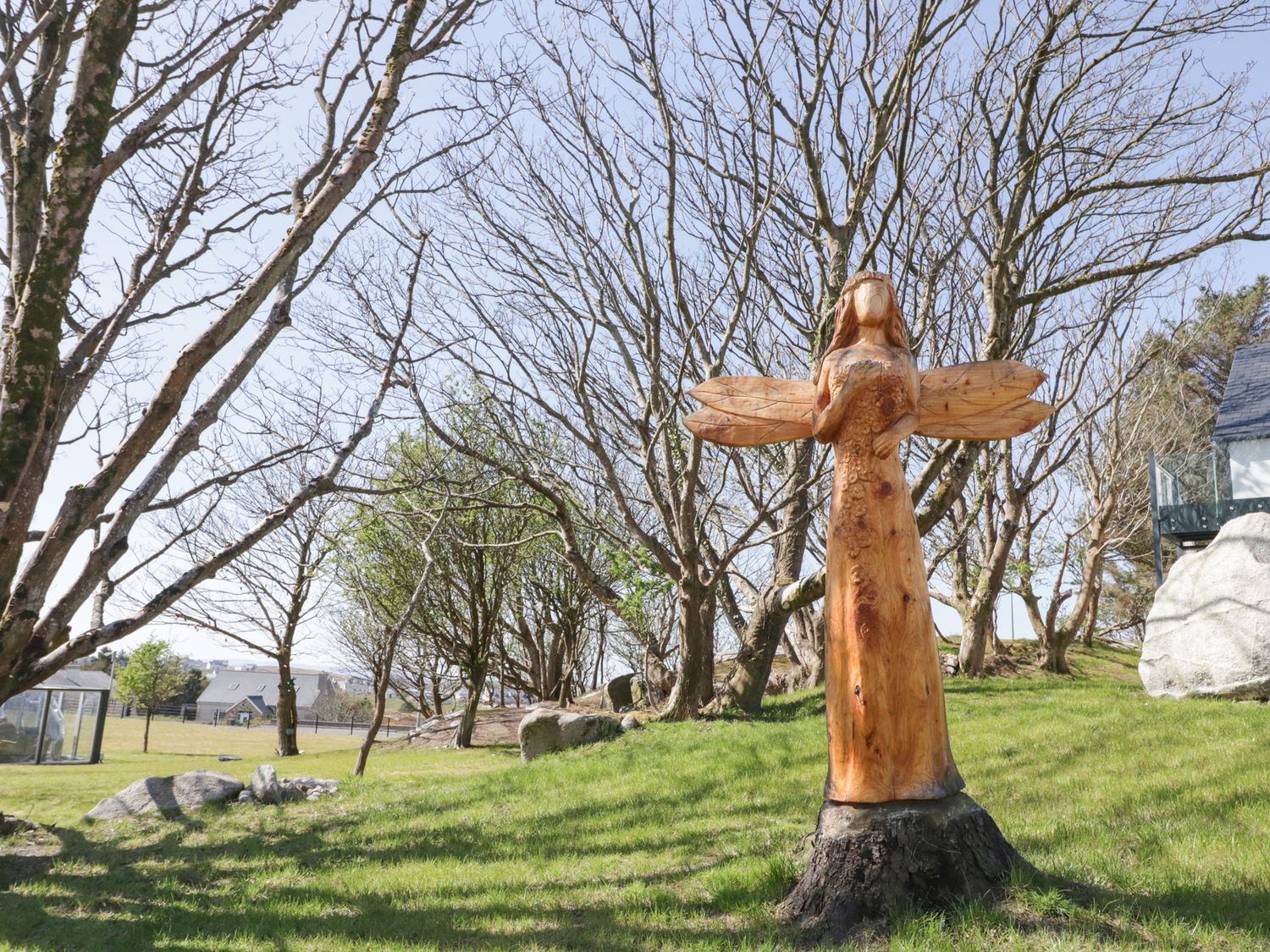 A wooden fairy statue with wings on a grassy area surrounded by leafless trees at Number 1 Dome in Derrybeg County Donegal