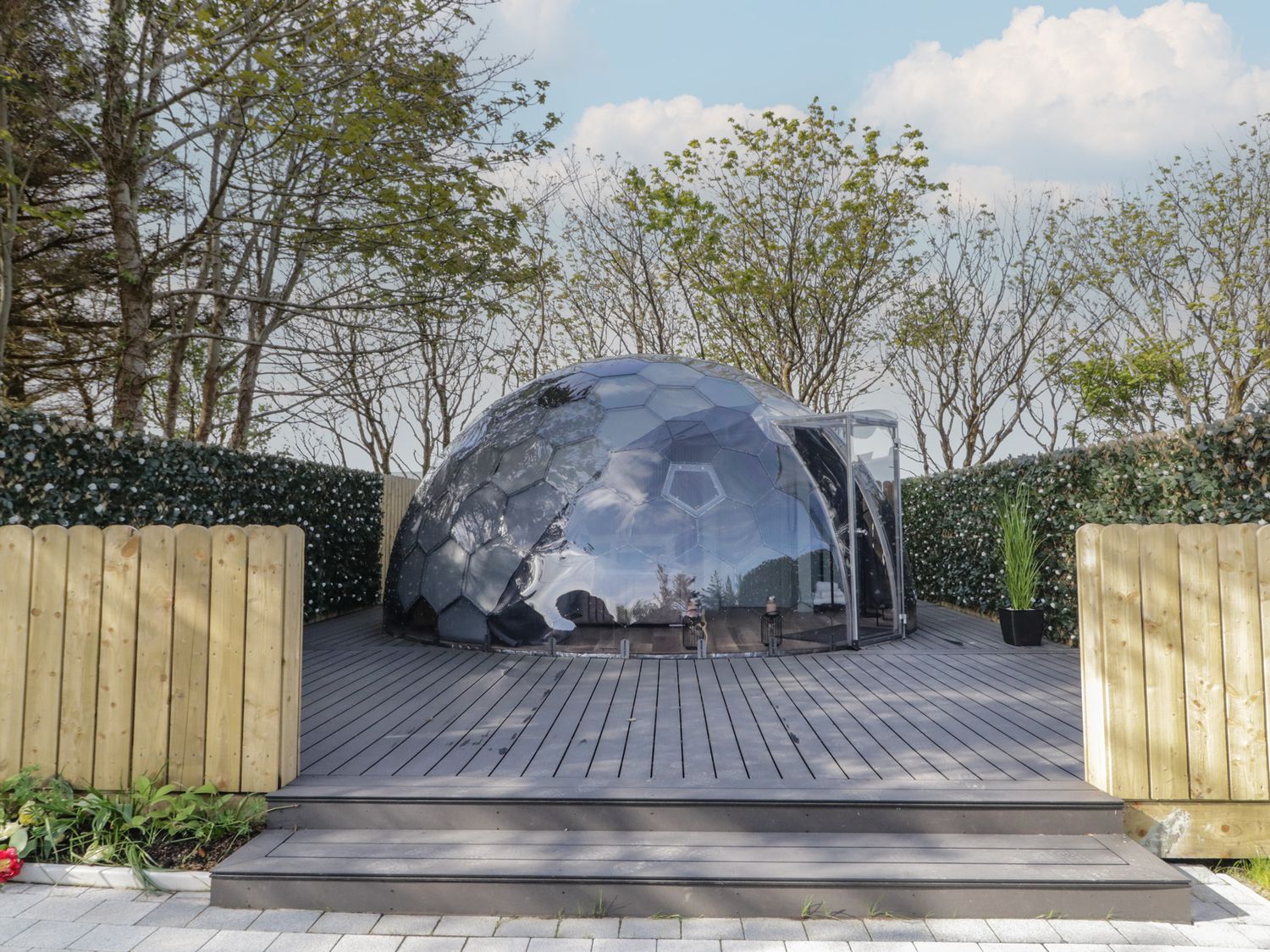 A transparent geodesic dome on a wooden deck surrounded by hedges and trees at Number 1 Dome in Derrybeg County Donegal