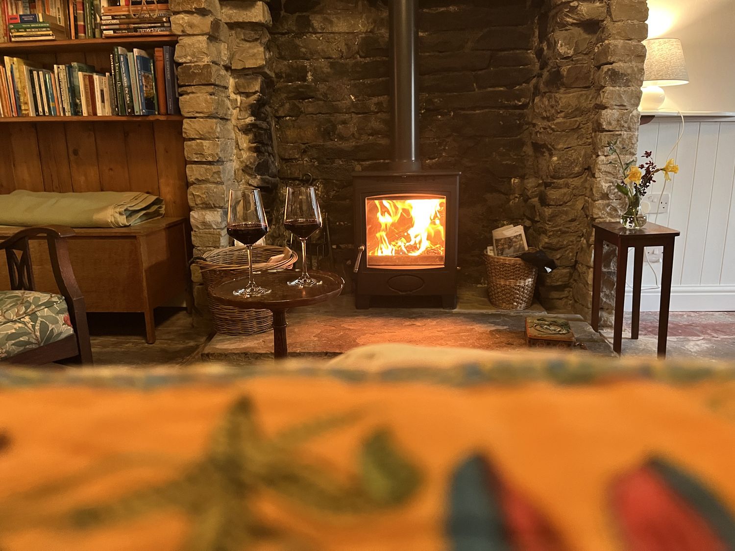 A living room with a wood burning stove and two glasses of red wine on a small round table at Doffers Cottage in Airton
