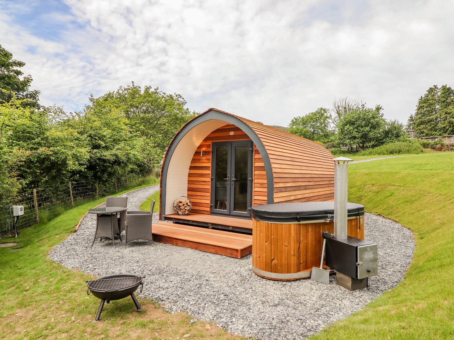 A wooden pod with glass doors next to a hot tub and outdoor furniture at Briallen in Bontddu near Dolgellau