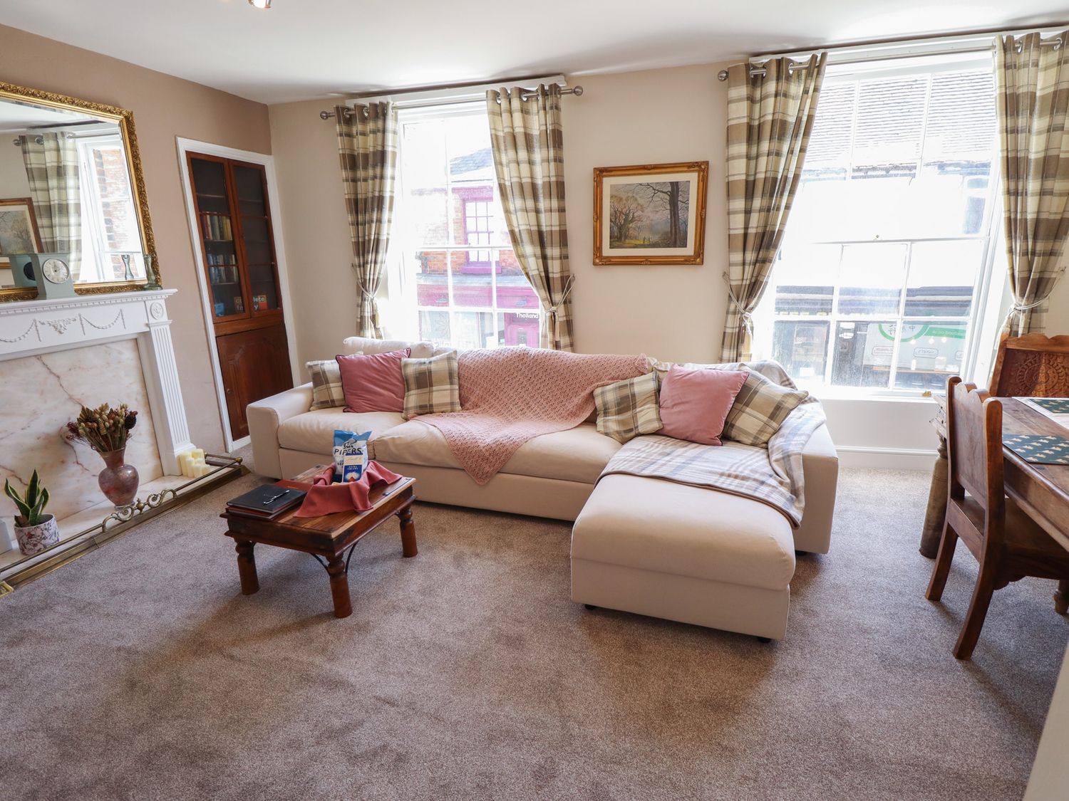 A living room with a beige sofa and cushions a wooden coffee table a fireplace and two large windows with plaid curtains at Madje Apartment in Lincoln
