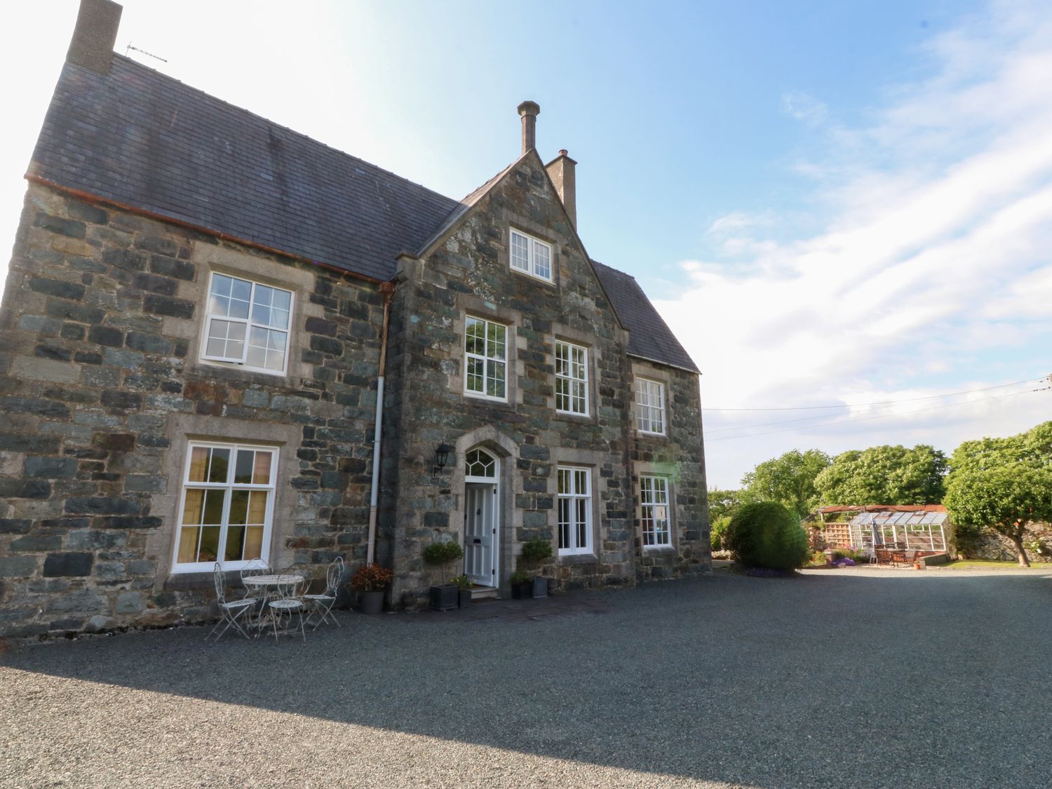 A stone house with white framed windows and a gravel driveway with a small outdoor table and chairs at Glasfryn in Llandwrog