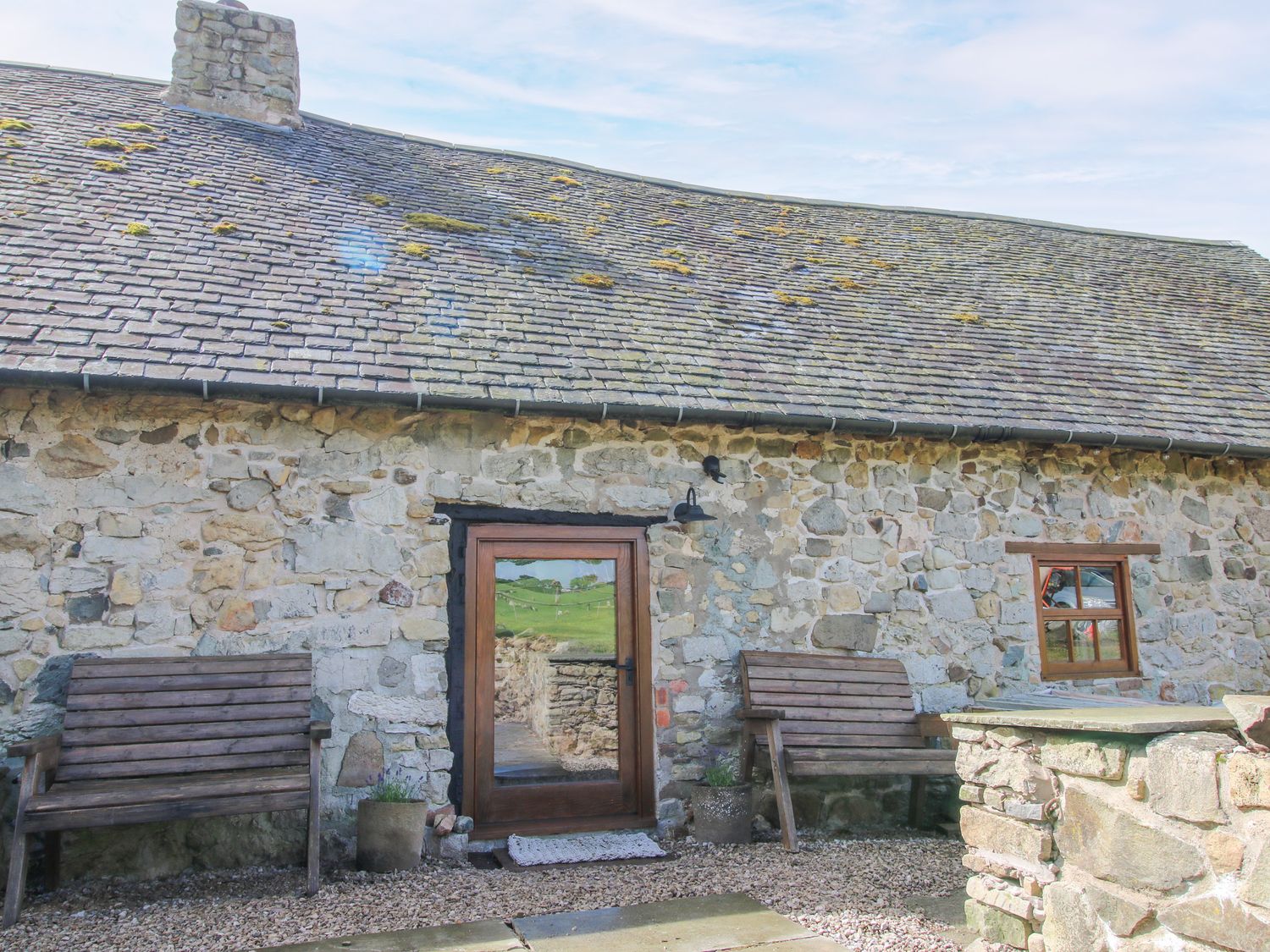 An outdoor area with a stone wall and benches at The Long House near Trefonen