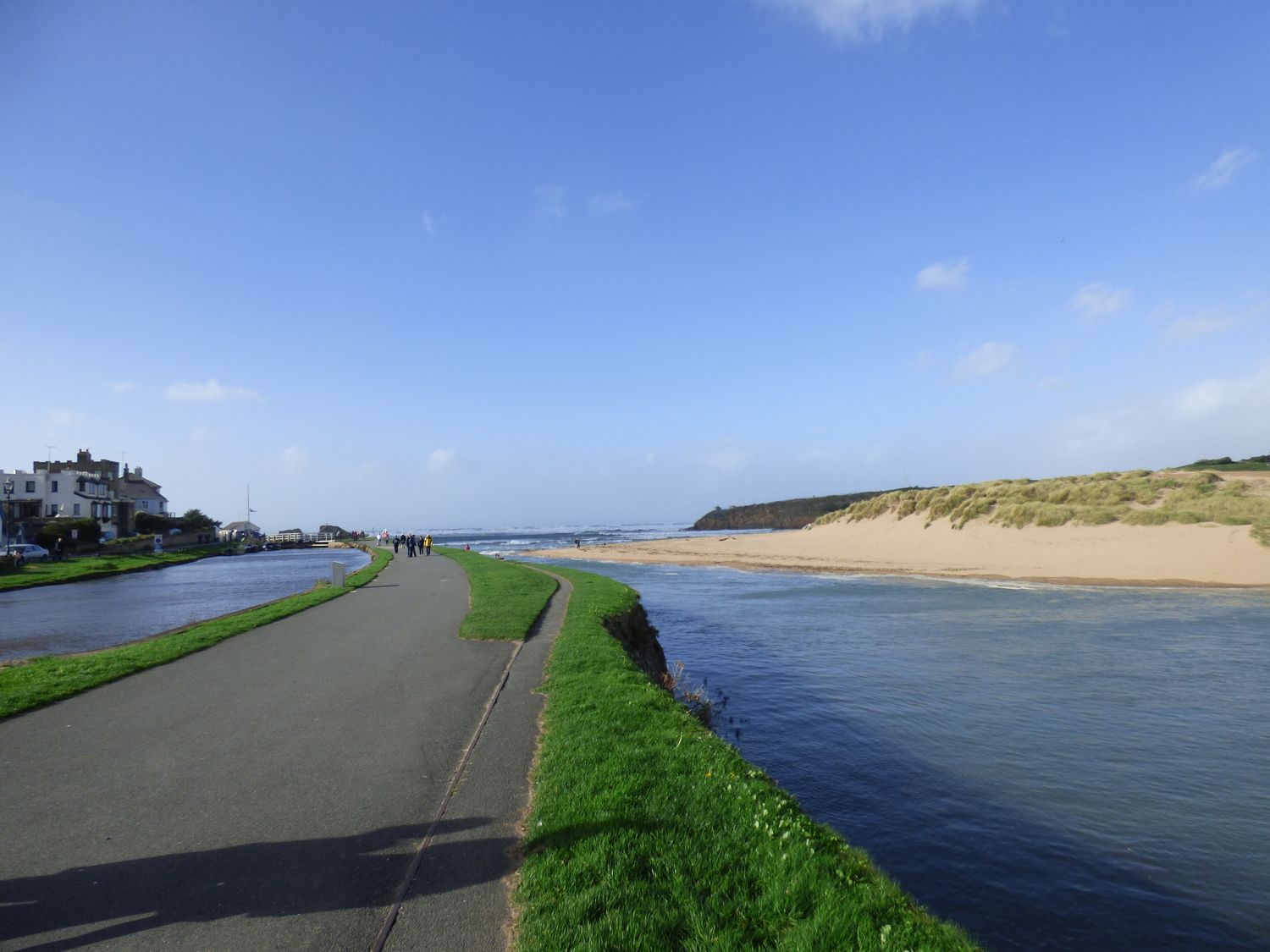 A paved pathway next to a river and a sandy beach with grass on the banks at Tea Cosy Cottage in Marhamchurch