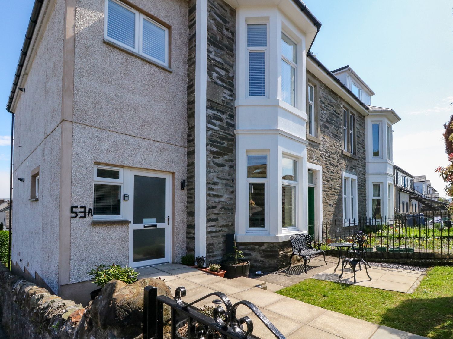 Front exterior of a stone and stucco house with a small garden area and metal outdoor furniture at Lenas Corner in Dunoon
