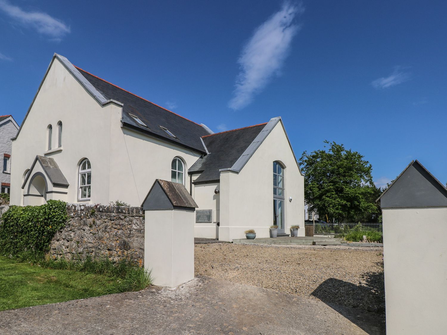 A white chapel building with a slate roof and arched windows surrounded by a low stone wall and open driveway at Zoar Chapel in Carew